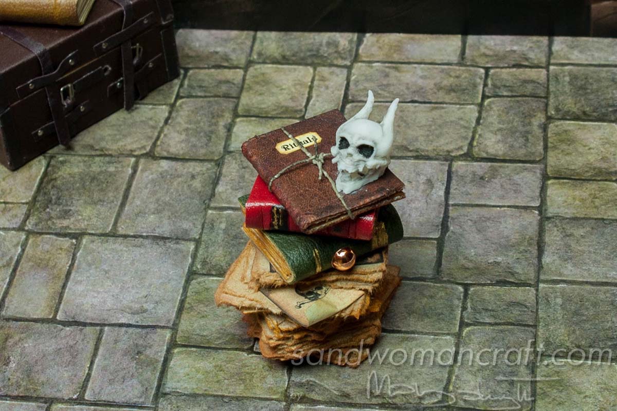 Miniature books stacked with monster skull and Rituals book